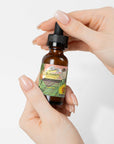 Moisturizing and strengthening hair oil in a brown glass bottle with a dropper, held in hand.